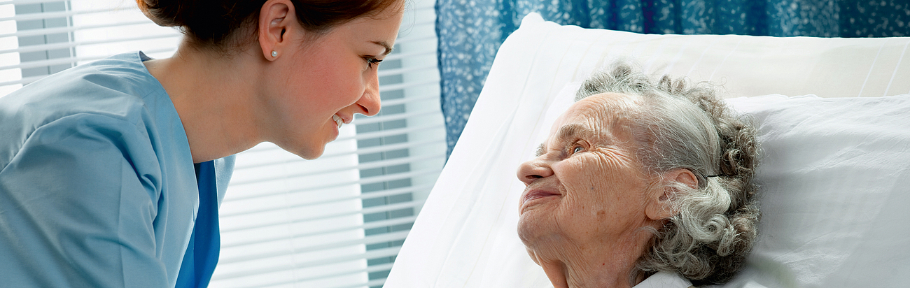 Freundlichkeit bei der Patientenbetreuung Pflegekraft mit älterer Dame am Krankenbett