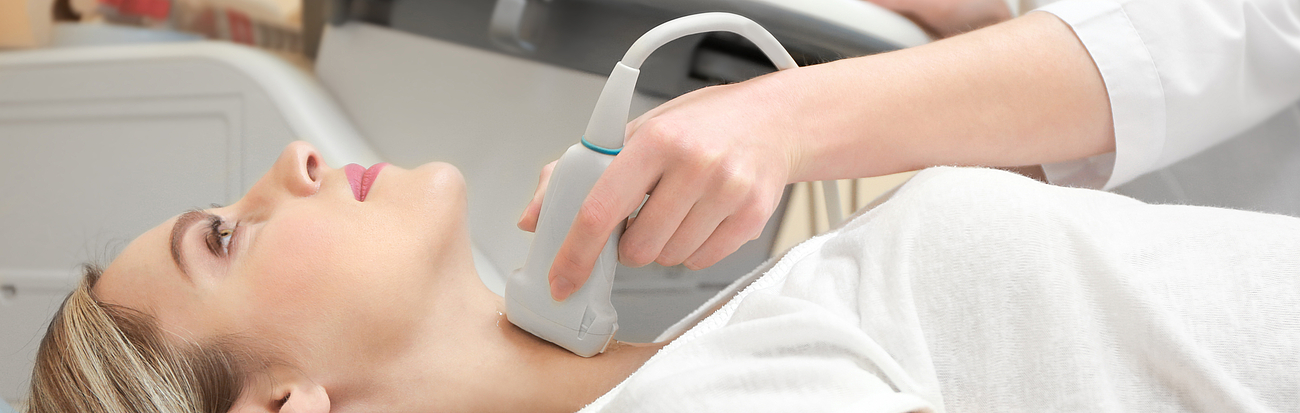 Ultraschall an der Schilddrüse Eine Patientin liegt auf einer Liege und die Schilddrüse wird mithilfe von Ultraschall untersucht.