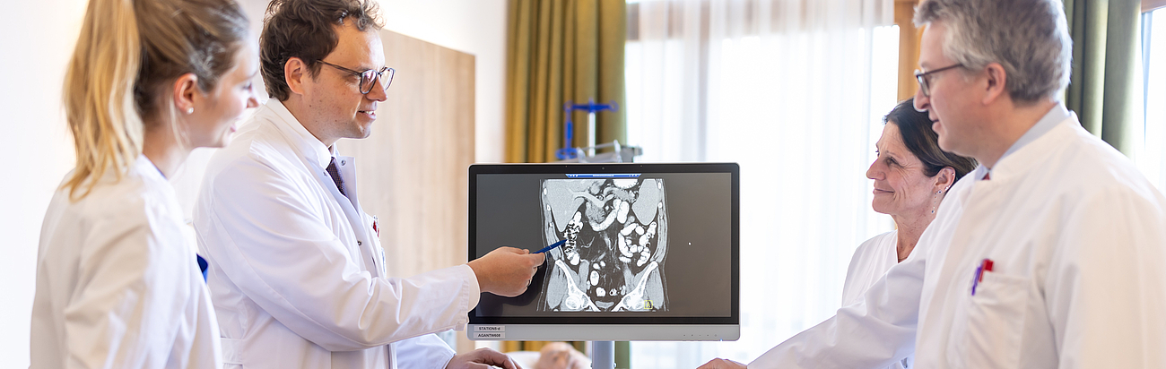 Ärzte unterhalten sich vor einem Computer im Stehen miteinander.