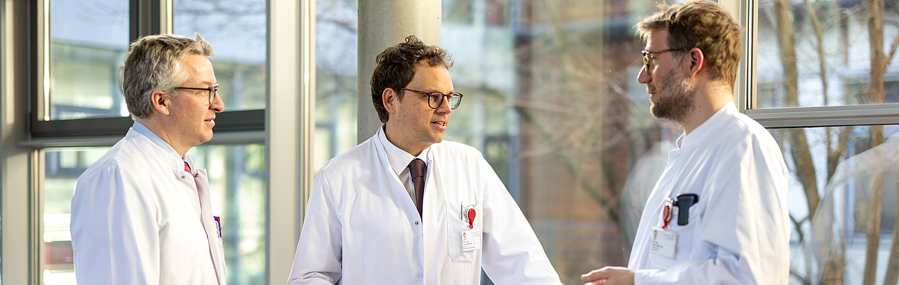 Ärzte unterhalten sich im Flur vor einem Fenster miteinander.