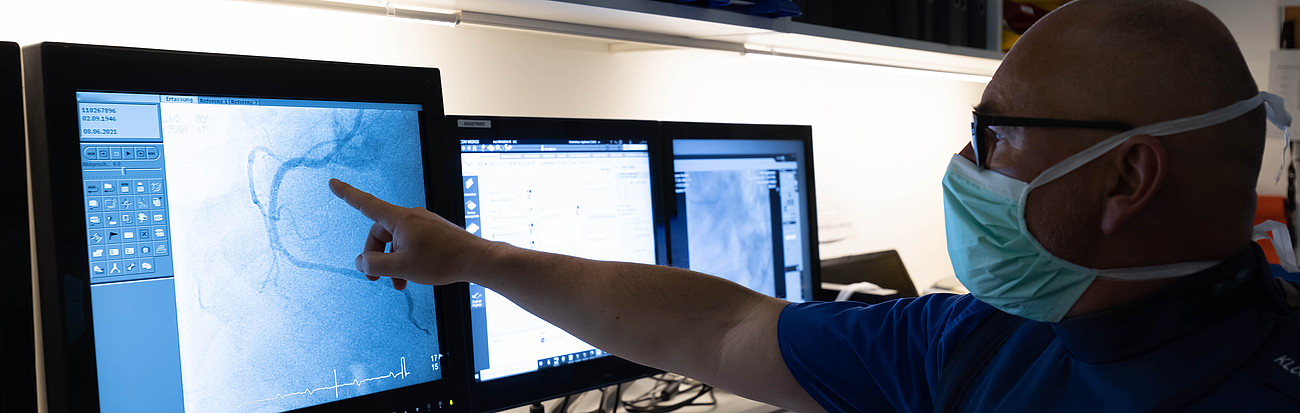 Ein Arzt mit Mundschutz sitzt vor Computern und schaut sich Untersuchungsergebnisse an.