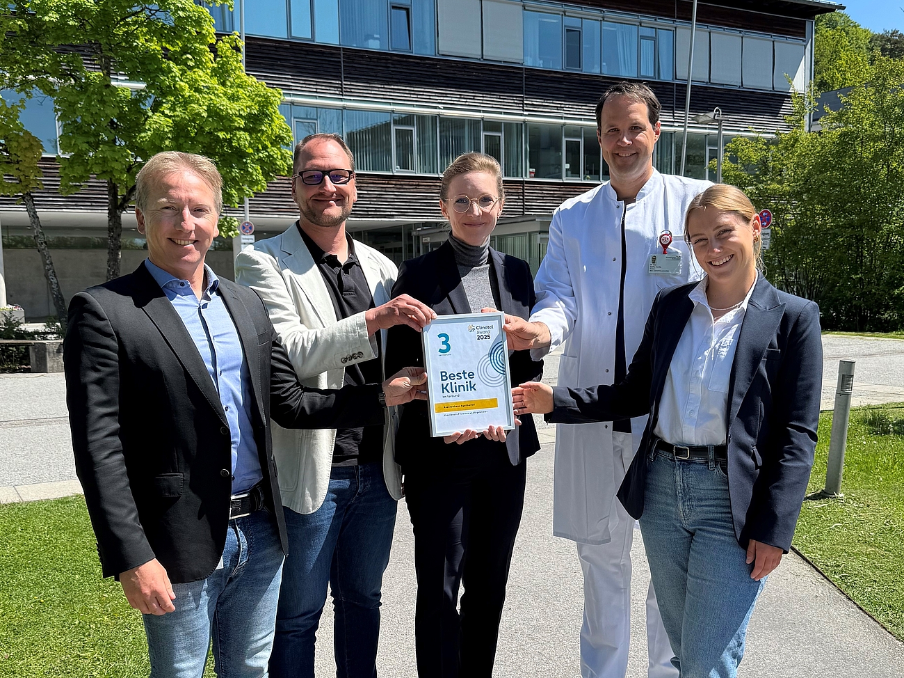 Die Klinikleitung steht draußen und sie halten eine Urkunde nach oben.