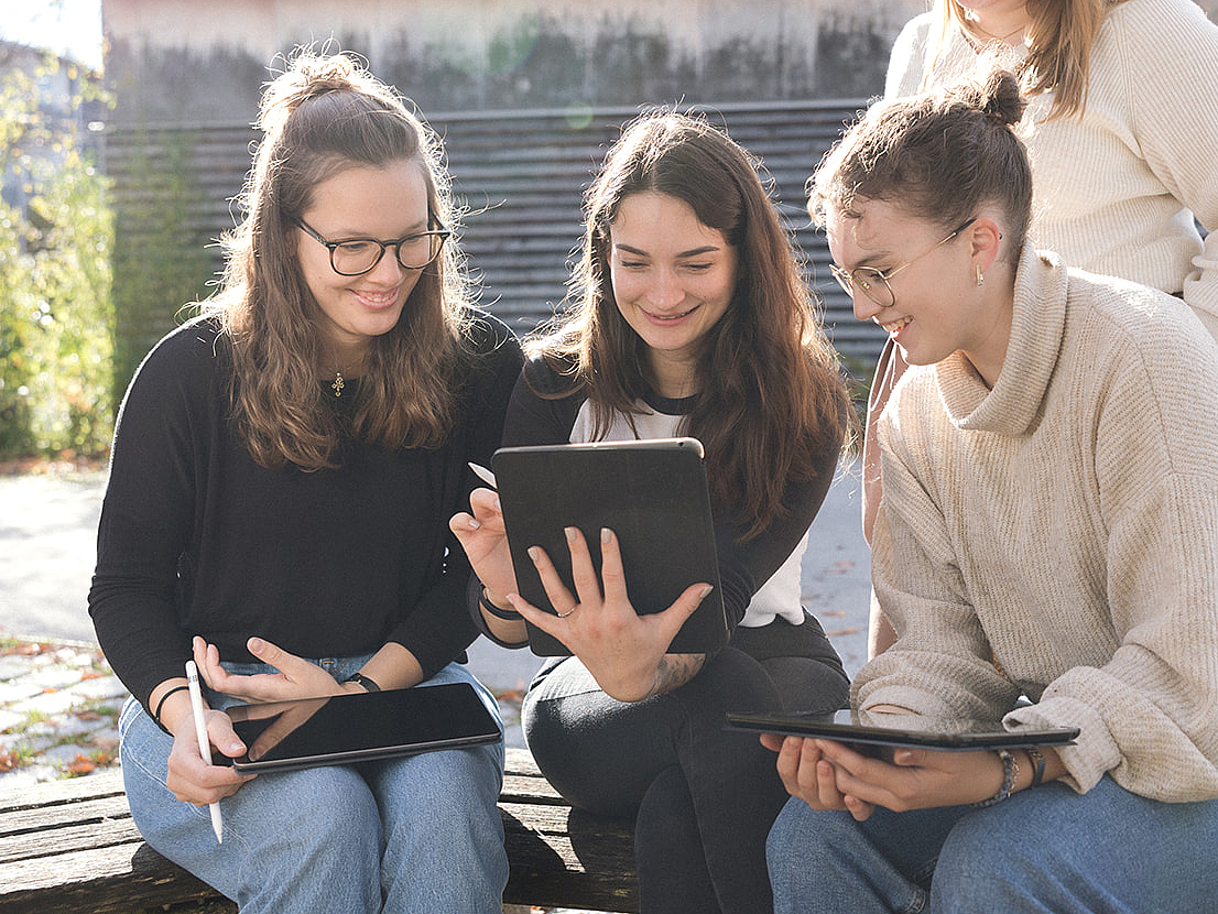 Schülerinnen sitzen vor dem Schulgebäude