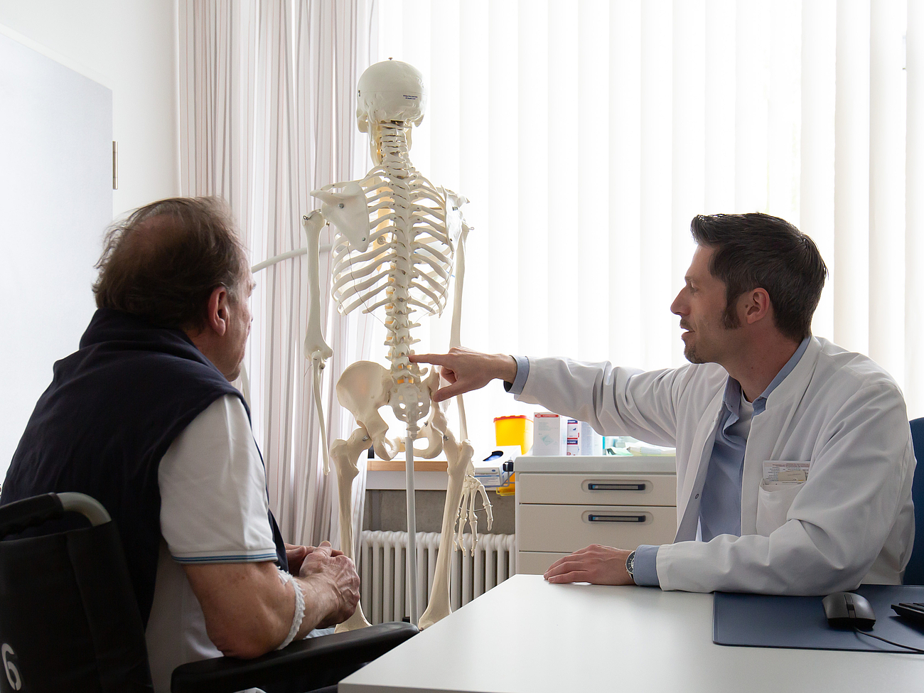 Neurochirurgische Sprechstunde Patient und Arzt betrachten Skelett-Modell